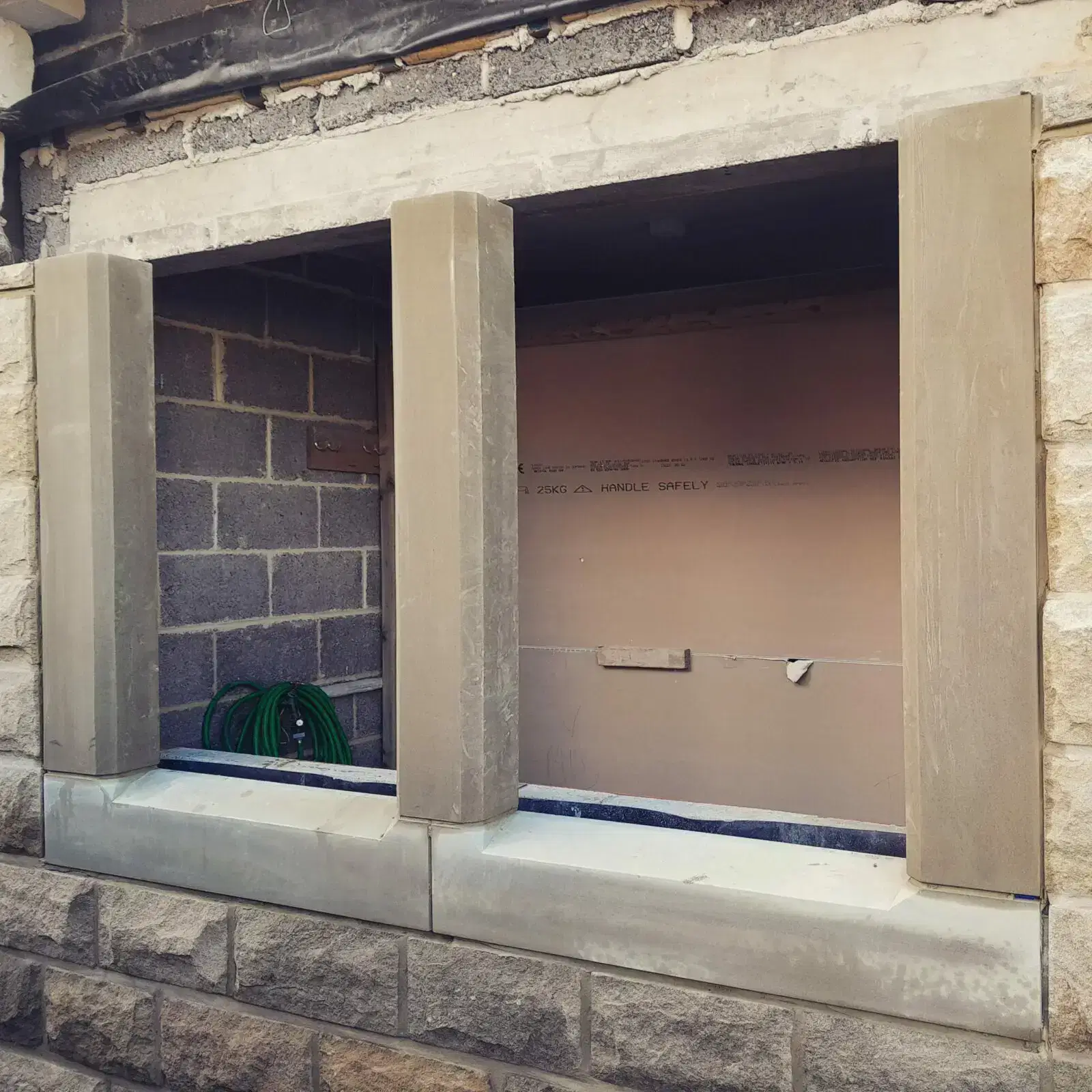 Newly installed stone window surround with ashlar masonry detailing on a residential building under construction.